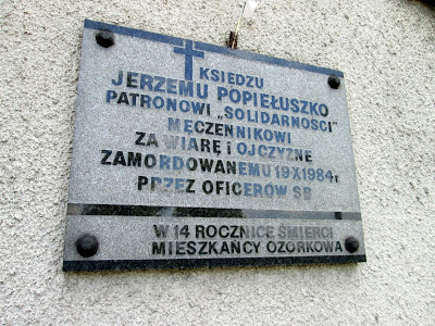 Tablica pamiątkowa ku czci ks. Jerzego Popiełuszki, zawieszona na frontowej ścianie kaplicy.